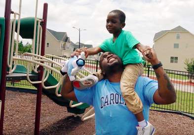 Mikhail Wright in a park, with his son on his shoulder holding a stuffed Rameses toy